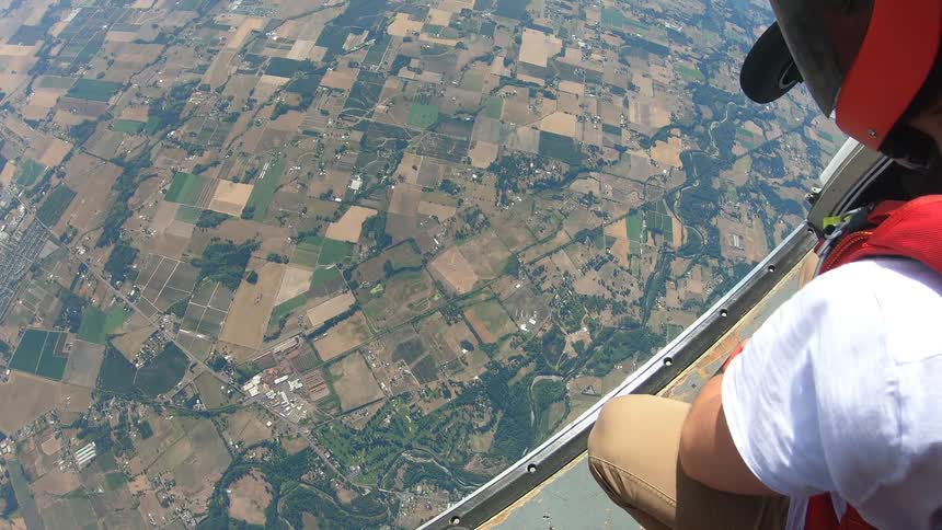 A man kneels on the edge of a helicopter and looks at the land below