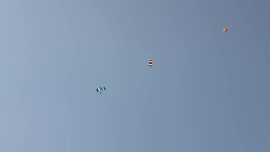 High above in the sky three parachutes are open and are slowly circling as they descend