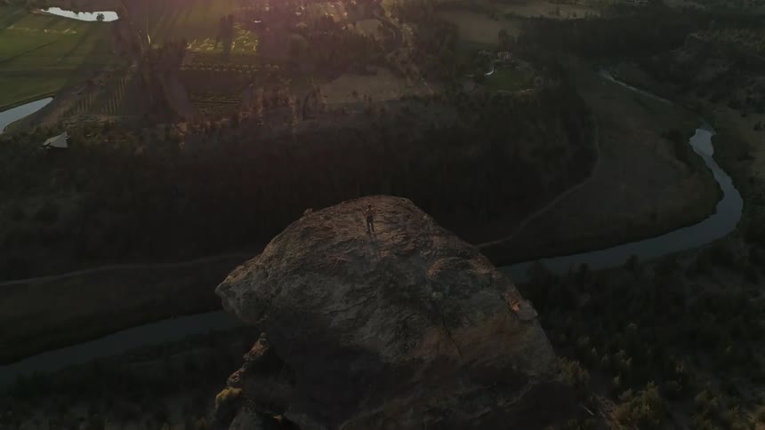 A person standing on a high hoodoo in the desert while looking at the green plains in the distance