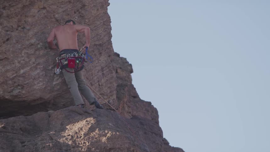 Shirtless man standing on ledge of rock while rock climbing