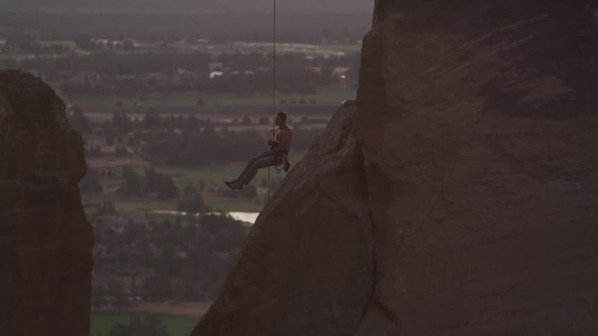 Man lowers himself down next to a mountain with a rope