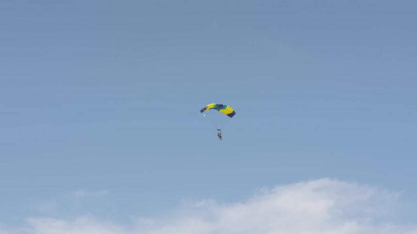 A skydiver gliding towards the ground beneath a parachute