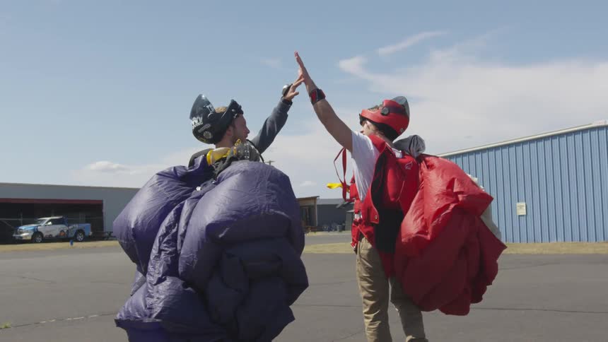 Two people with deployed parachutes high fiving