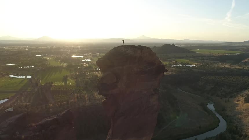 Person standing high upon a unique rock formation at sunrise
