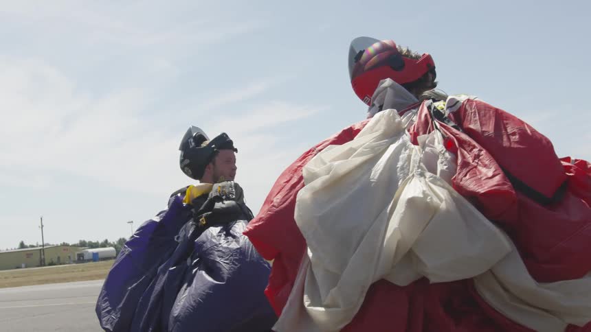 A man and woman walk along carrying parachutes
