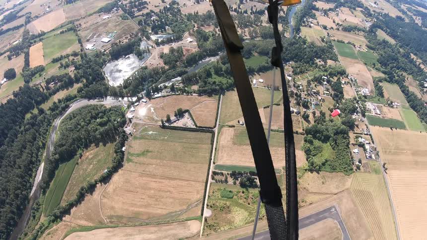 A pair of skydivers with their parachutes released gliding down towards the countryside below