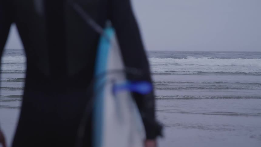 Man in wet suit holding surfboard looks at the sea on the beach