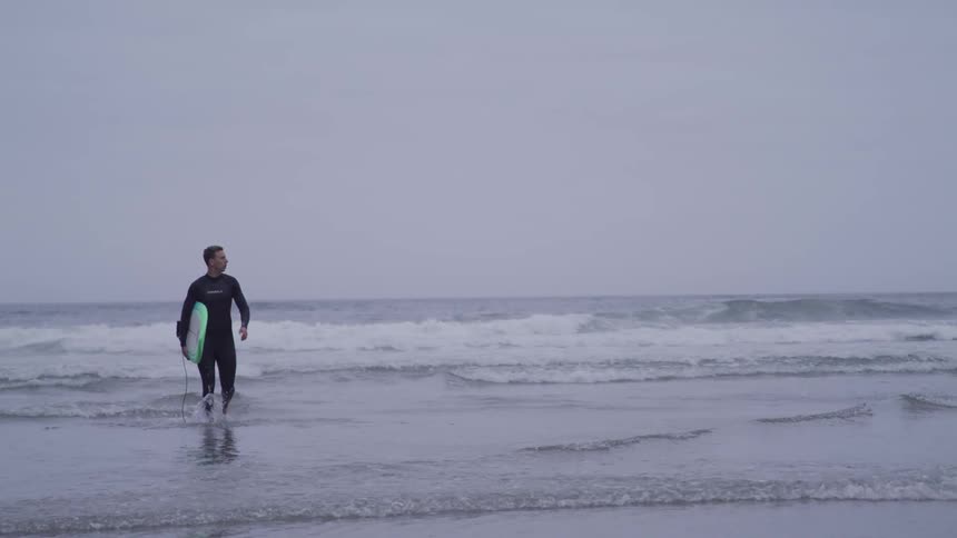 A man carries a surfboard from the ocean towards the beach