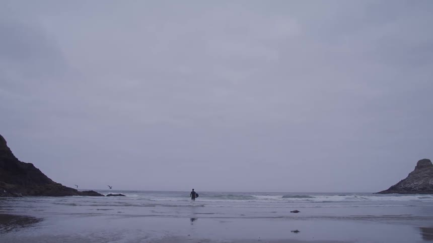 Man in swimsuit holding surfboard goes swimming on cloudy day