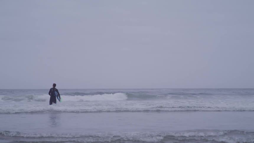 A man runs in to the ocean with a surfboard