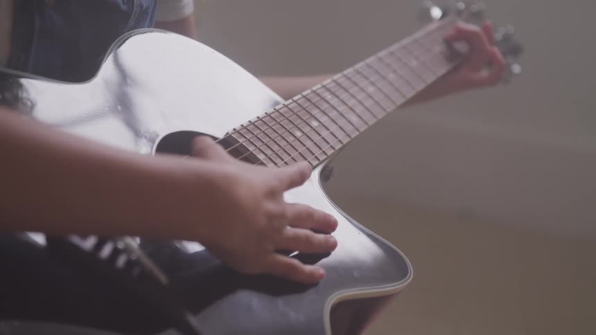 Person plays a guitar in a room during daylight