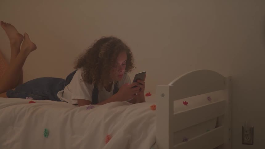 A curly woman play with her phone at the bedroom