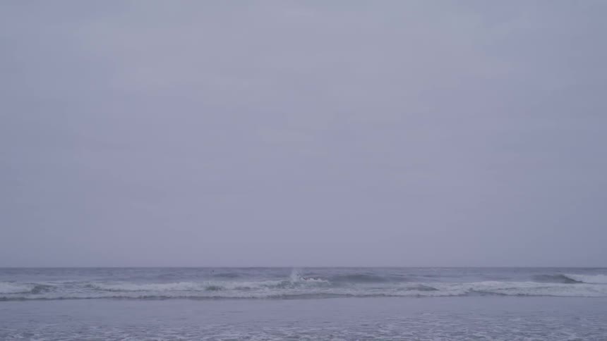 Man in wet suit holding surfboard goes swimming on cloudy day