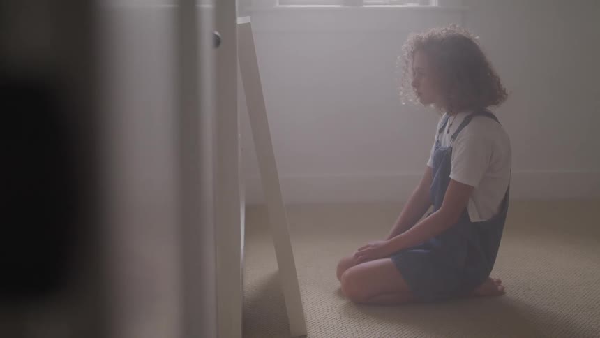 A young girl kneels in front of a mirror