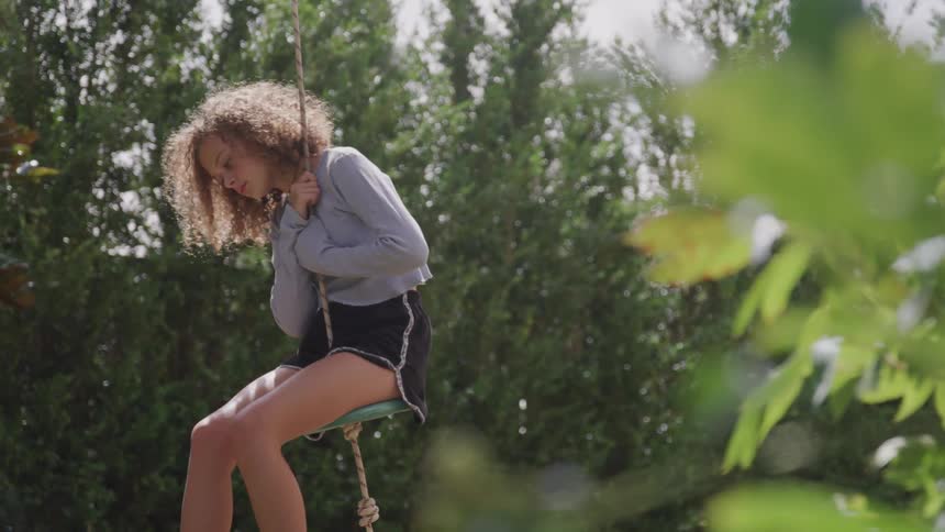 Girl with curly hair swinging on a swing
