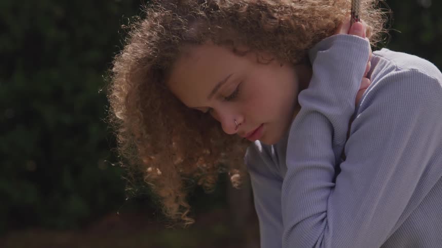 A teenage female with a nose piercing is holding onto a rope while gently swinging