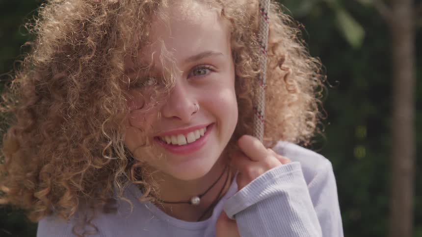 A young girl smiles as she hangs onto a rope