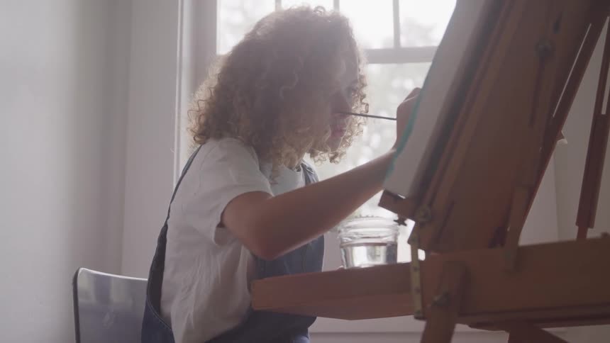 Girl painting on canvas sitting in front of window
