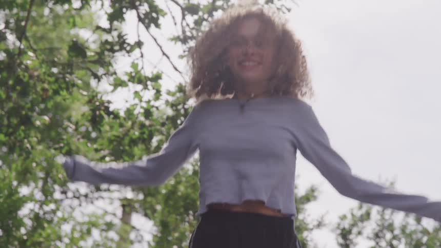 Curly red hair girl jumps under the tree during the day