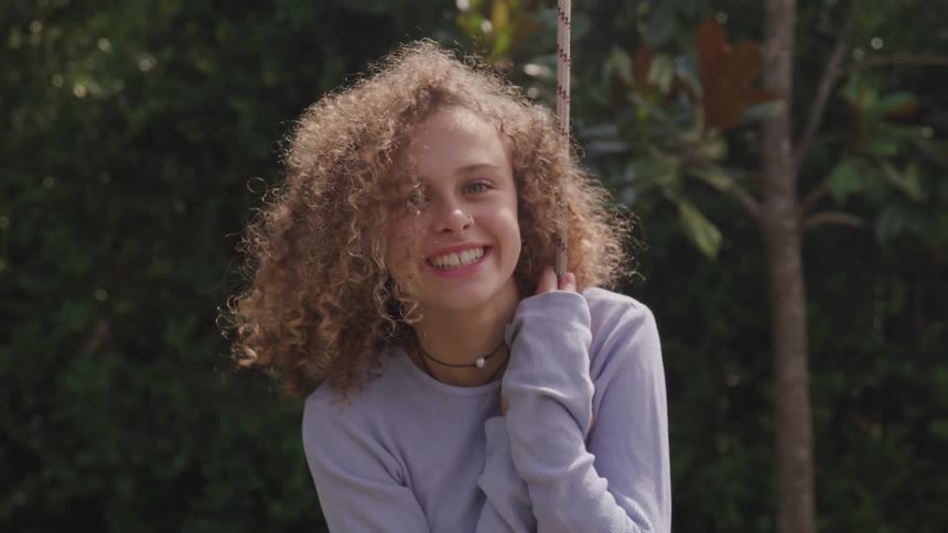 A girl holding onto a rope then looking up and smiling