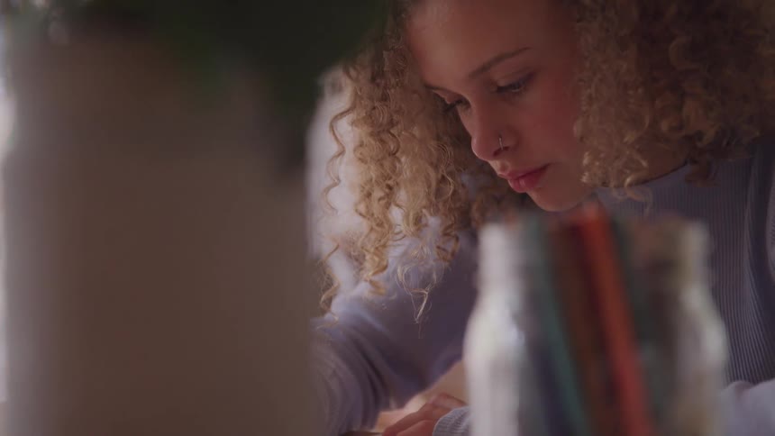 Curly red hair girl sitting at the table draws on the paper in a room