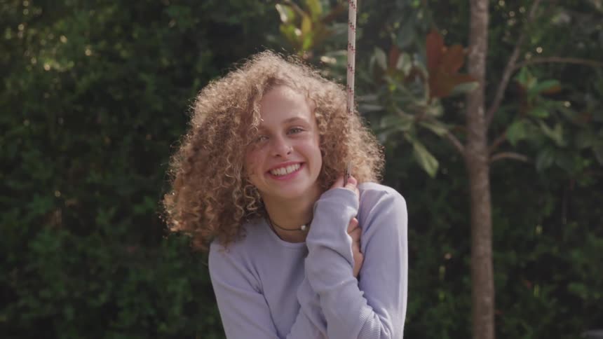 A young woman raising her head to smile into the camera while leaning on a rope