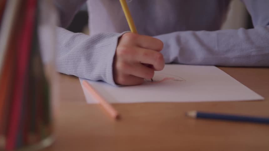 Boy draws on a piece of paper with a pencil