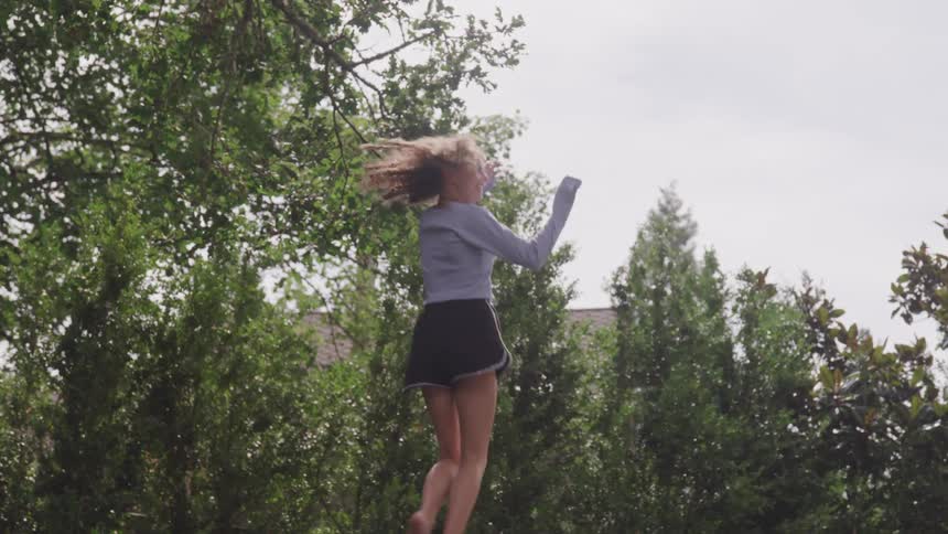 A young girl jumps outside on a trampoline
