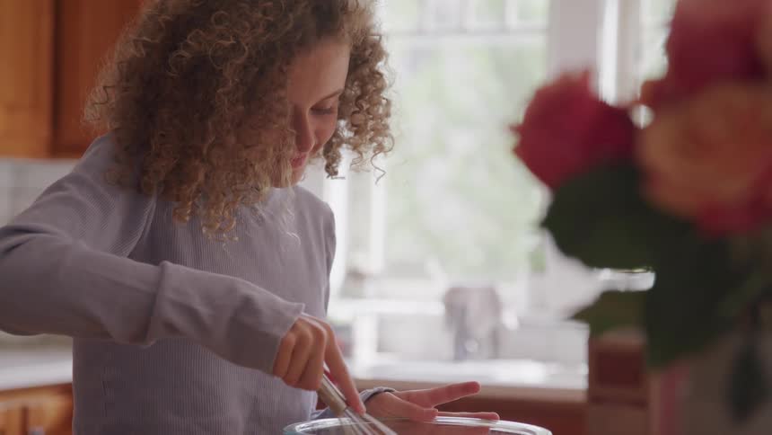 A young girl smiles as she stirs ingredients in a clear glass bowl with a whisk