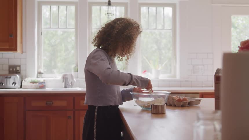 Woman with curly hair using a whisk to stir ingredients in a bowl while preparing to make some food