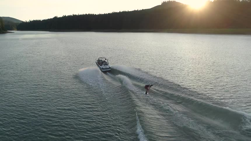 A person water skis behind a boat and makes a big jump over a wave