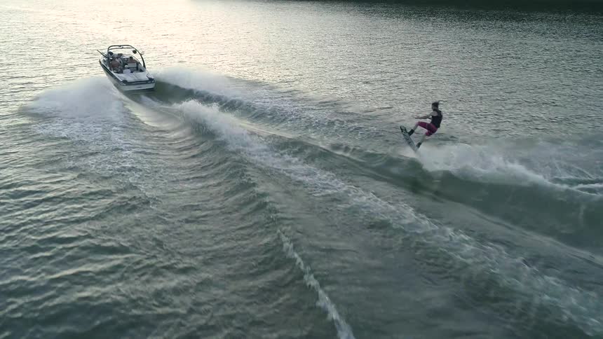 Wakeboarder jumping and turning over a wake while being pulled by a boat