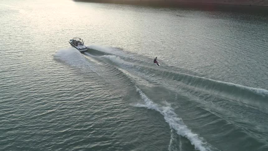 Man water skiing and jumping the waves created from the boat pulling him near sunset