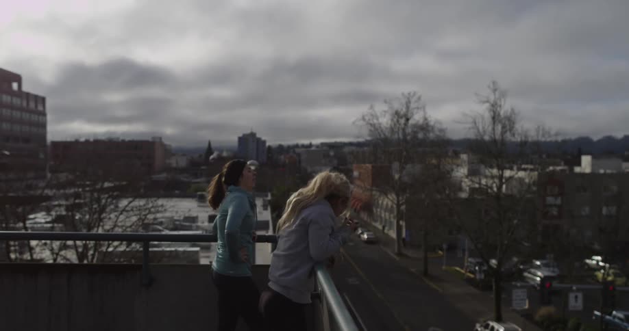 Two ladies run on top of a building and look over the edge