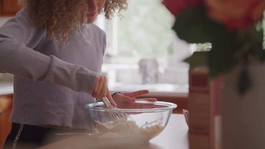 Girl at kitchen using whisker to mix flour in bowl