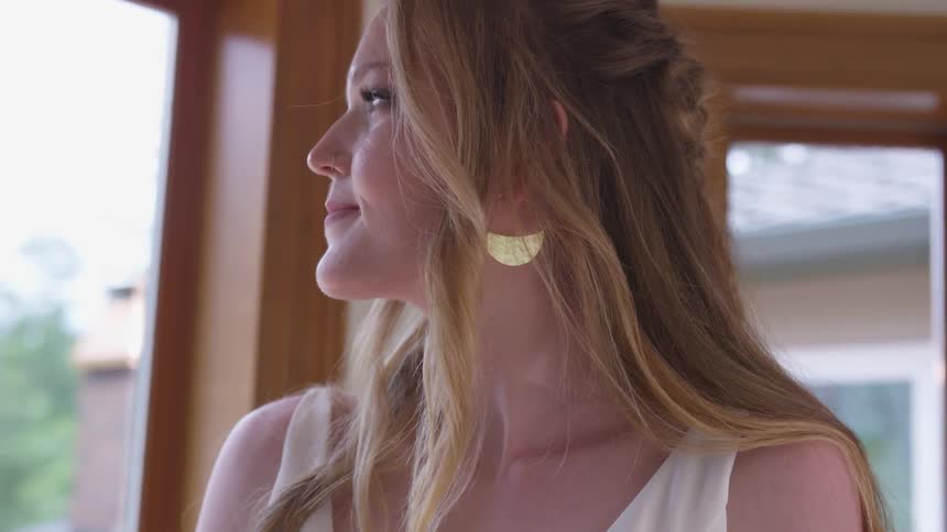 A woman puts an earring in her ear while staring out a window