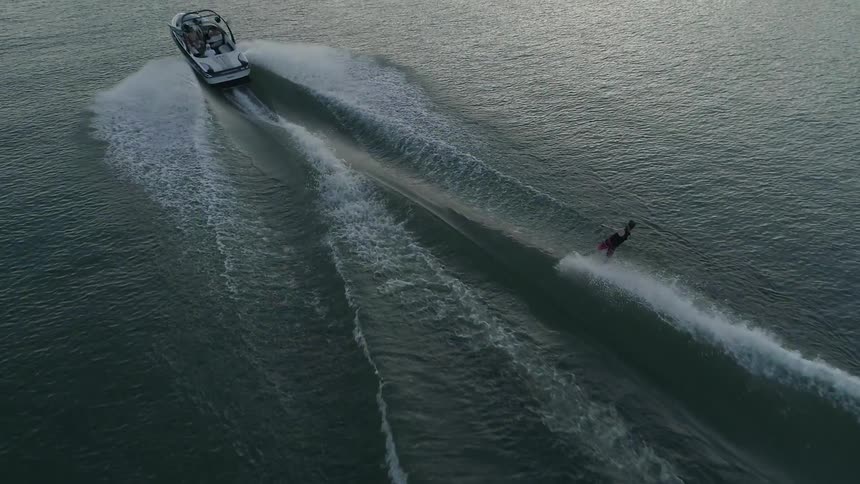 A person riding on a wakeboard is towed behind a fast moving motorboat