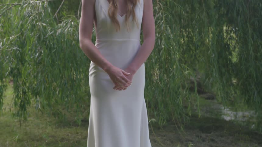 A woman wearing a wedding dress standing in front of a willow tree