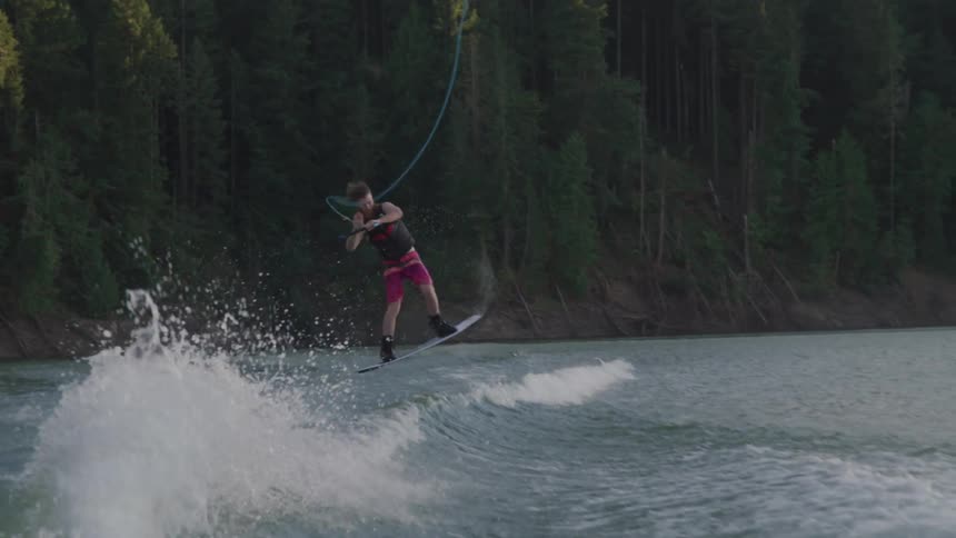 Wake boarder jumping then twisting over a wave and falling in lake