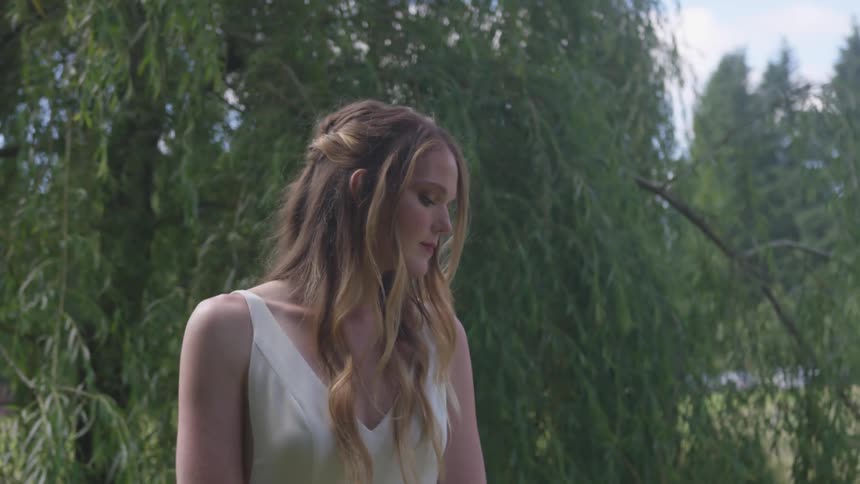 A woman is standing outside by the trees looking down