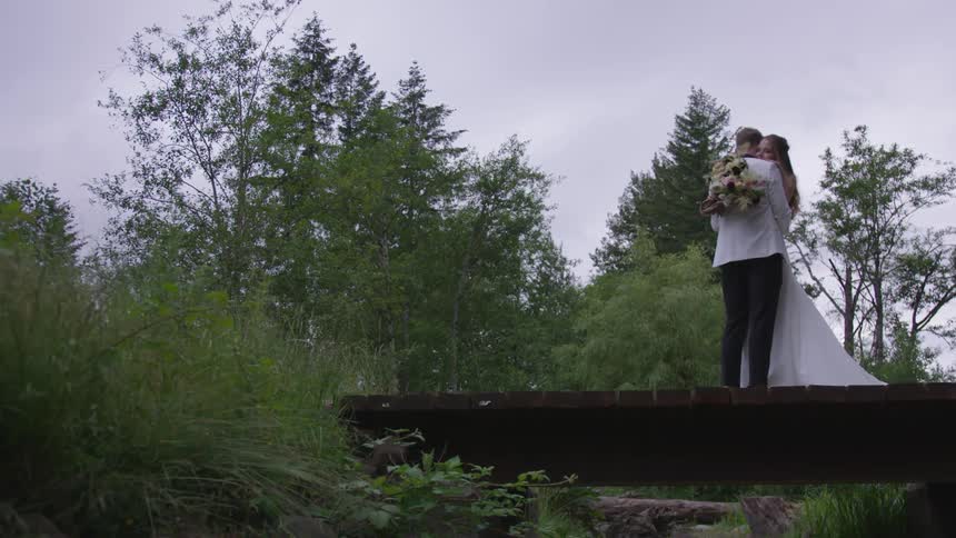 Groom and bride cuddle each other on the wooden bridge in the woods