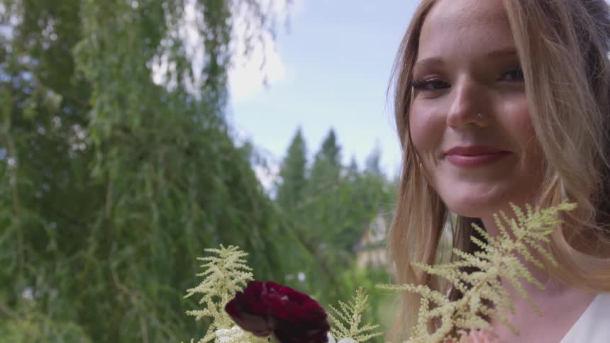 A woman smiling into the camera while standing outdoors holding plants