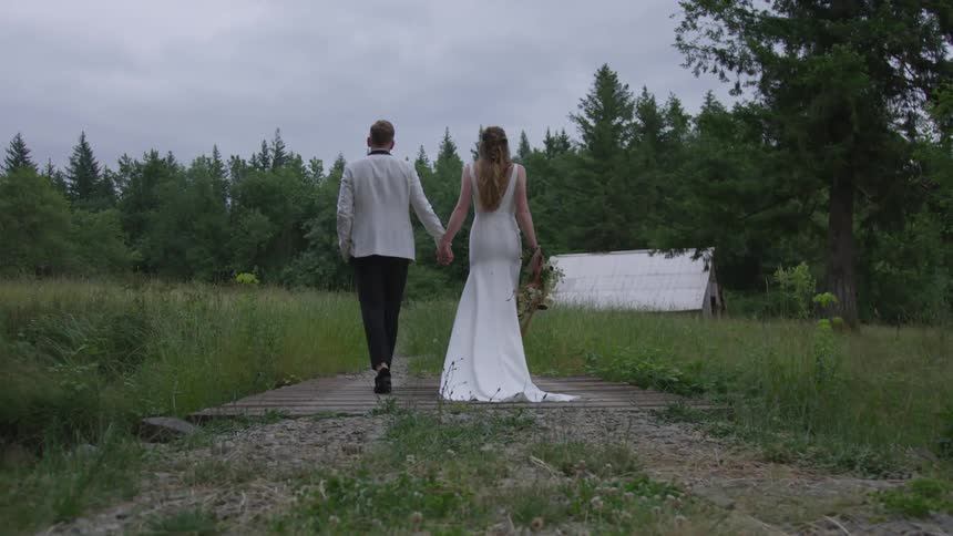 A bride and groom hold hands as they walk down a gravel trail
