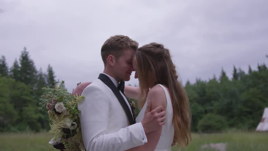 Wedding couple posing outdoors in a field with forest as the background