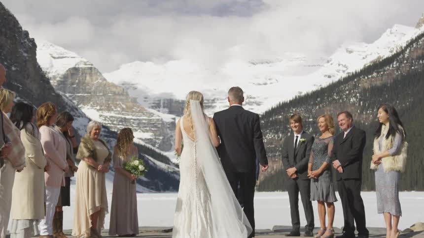 Bride walks down the aisle escorted by her father as a group of people watch