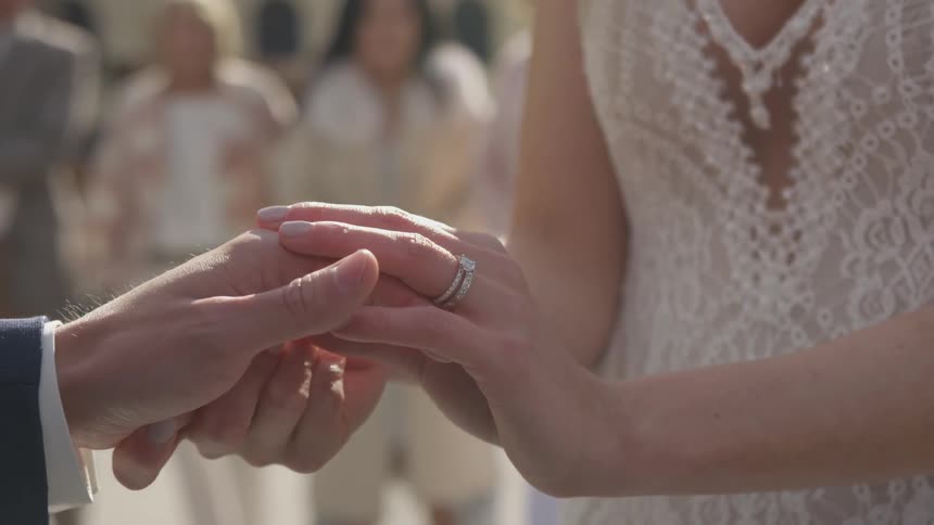 A bride and grooms clasped hands as they get married outside with family and friends looking on