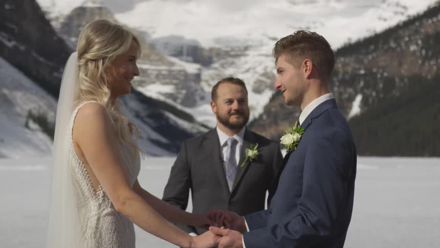 Bride and groom face each other hand in hand in front of the officiant and a snow covered mountain