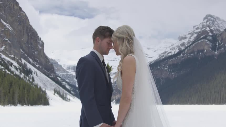 Bride and groom stand close together near the snow covered mountains