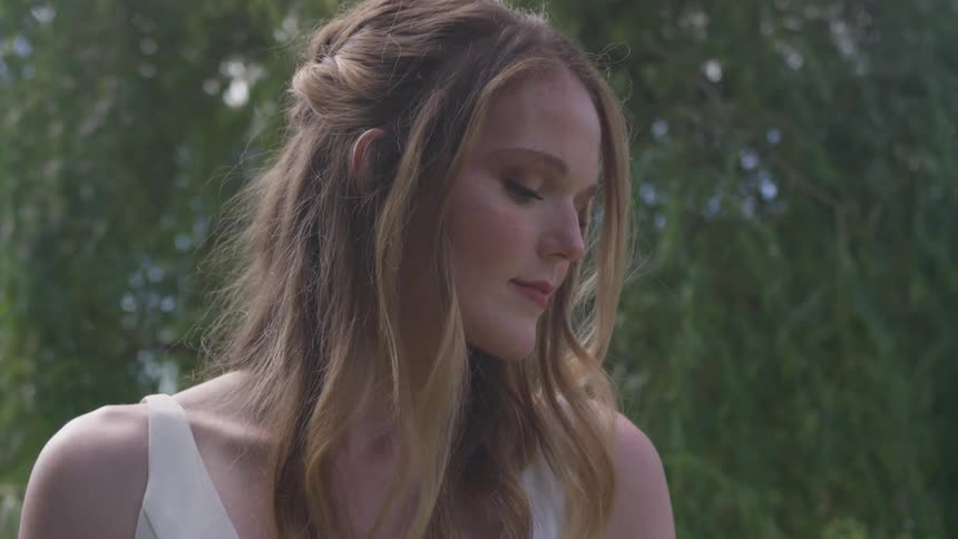 Bride stands and looks down at the groundin the woods