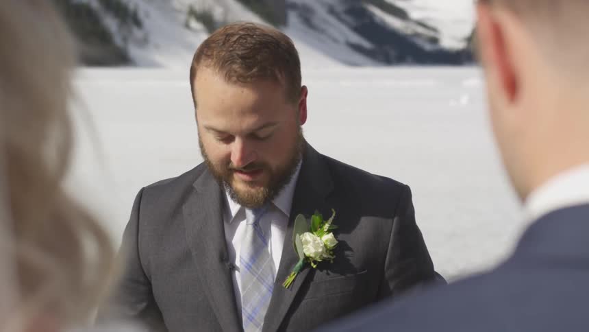 A man stands in front of a bride and groom and reads to them